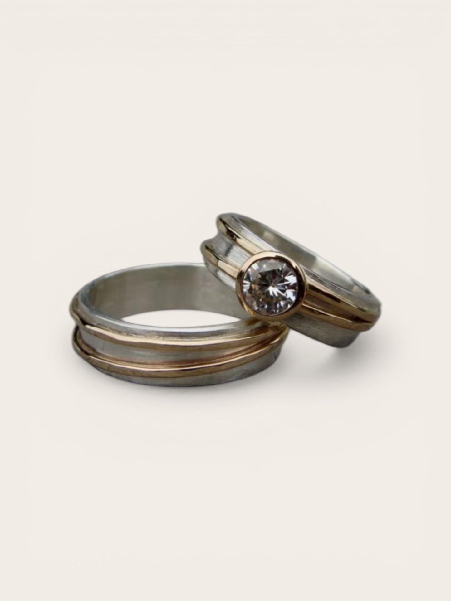 Two metallic rings with one featuring a diamond on a light gray background