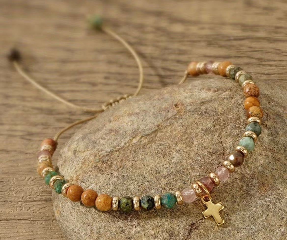 Beaded bracelet with a cross charm on a stone surface