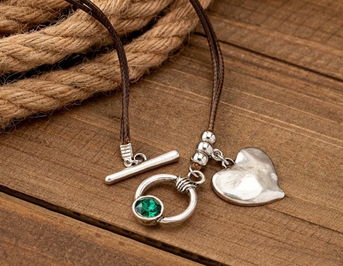 Silver necklace with heart and green gemstone pendant on a wooden surface