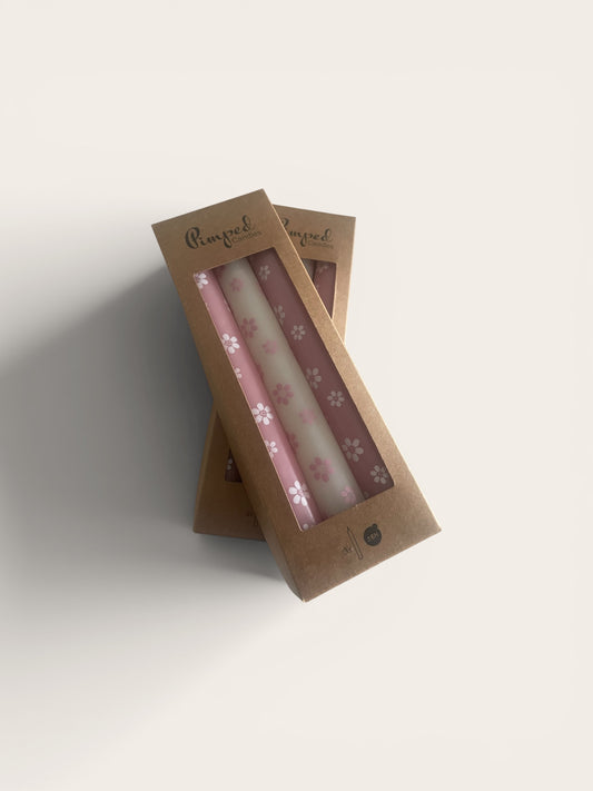 Two pink candles with floral design in a cardboard packaging on a light gray background