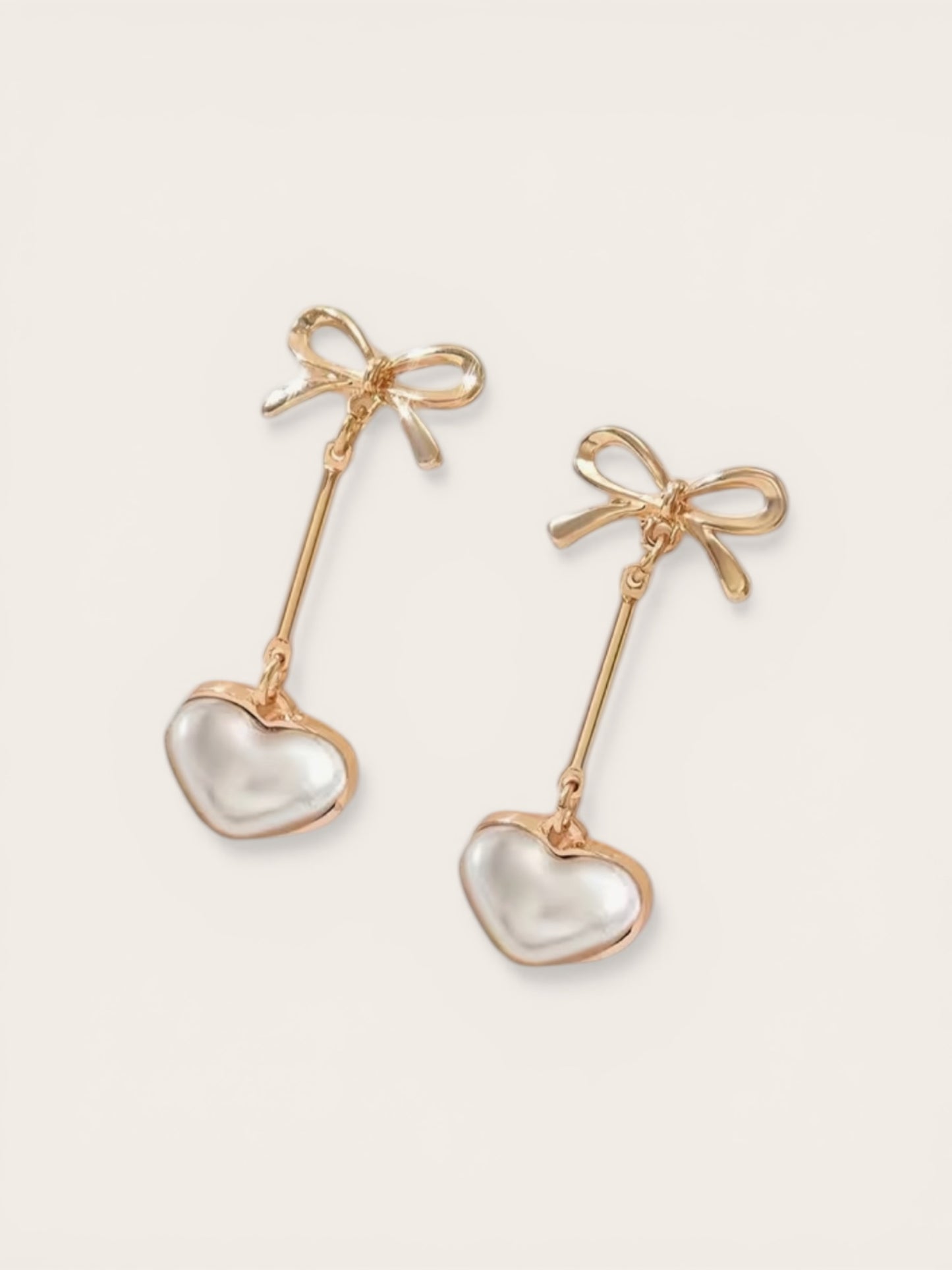 Gold earrings with heart-shaped charms and bow details on a white background