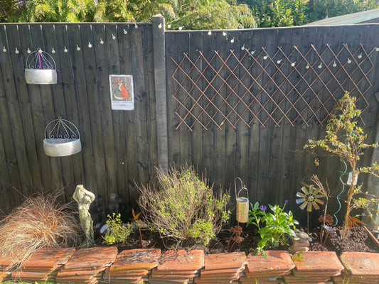 Rustic garden fence decorated with botanical plaques and bird ornaments surrounded by cottage garden plants
