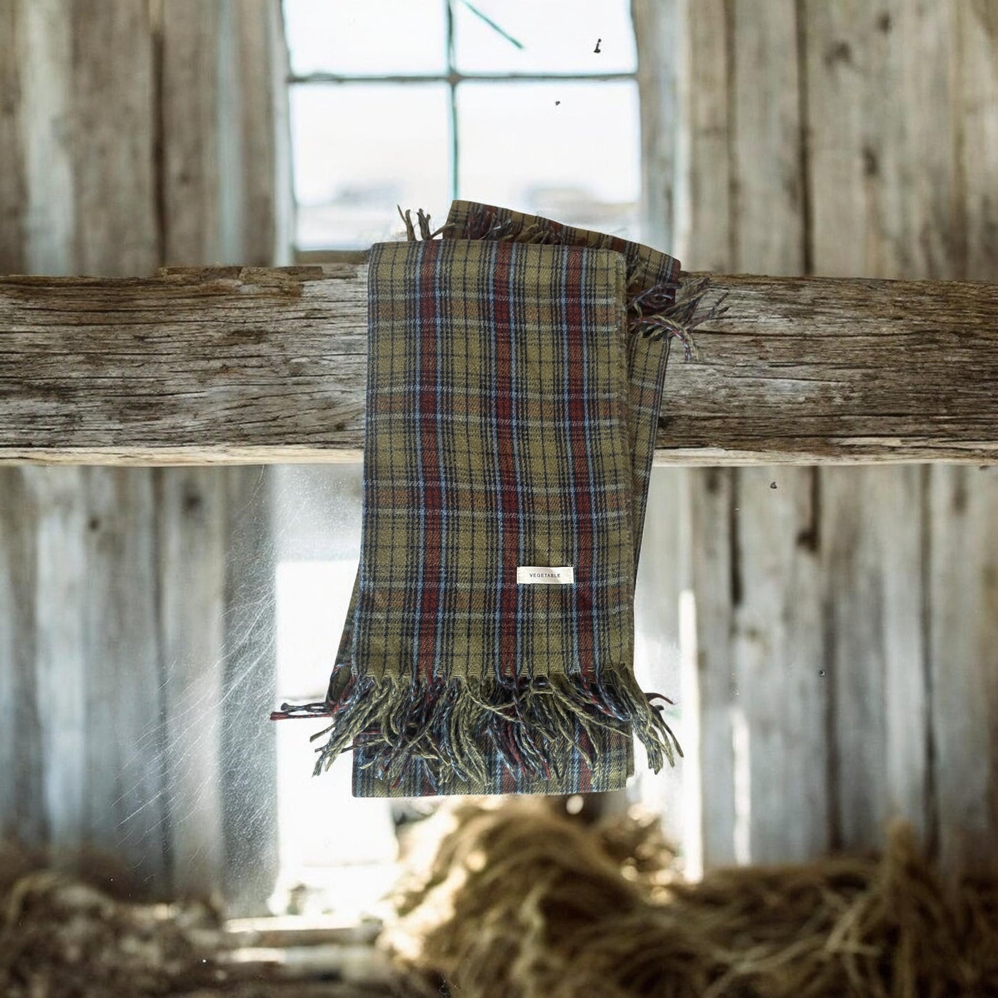 Plaid blanket with fringes draped over a wooden beam in a rustic setting