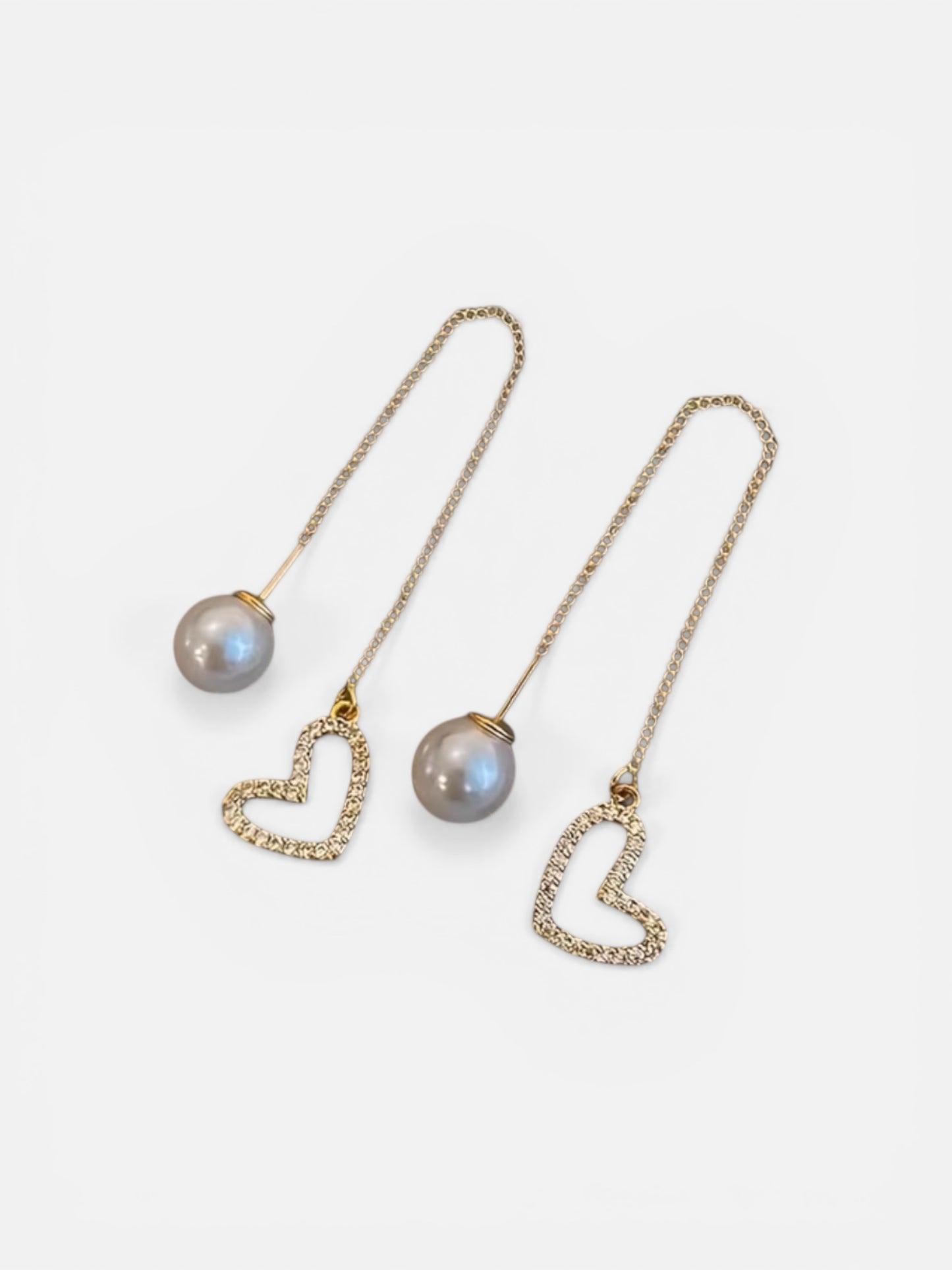 Pair of pearl earrings with heart-shaped clasps on a light background