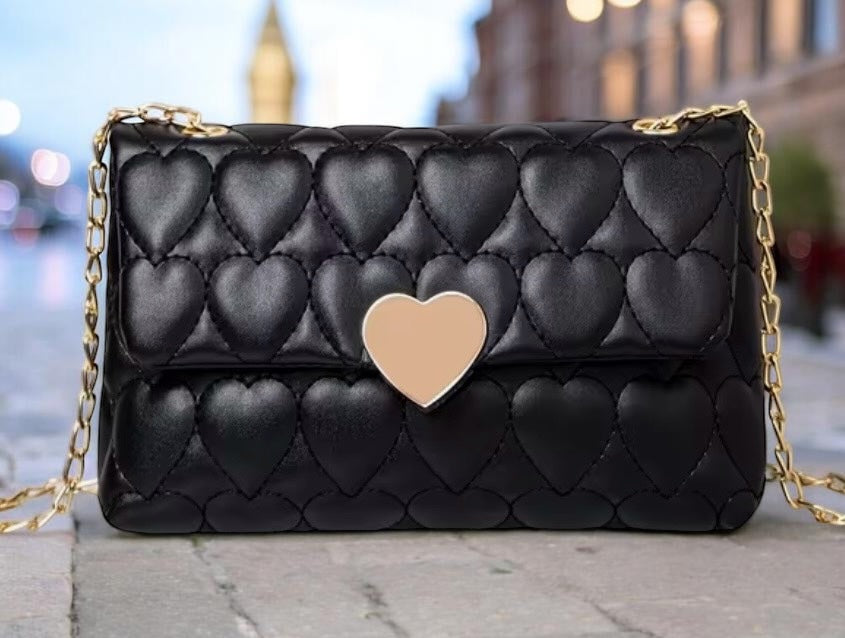 Black quilted handbag with a gold heart detail on a blurred city street background