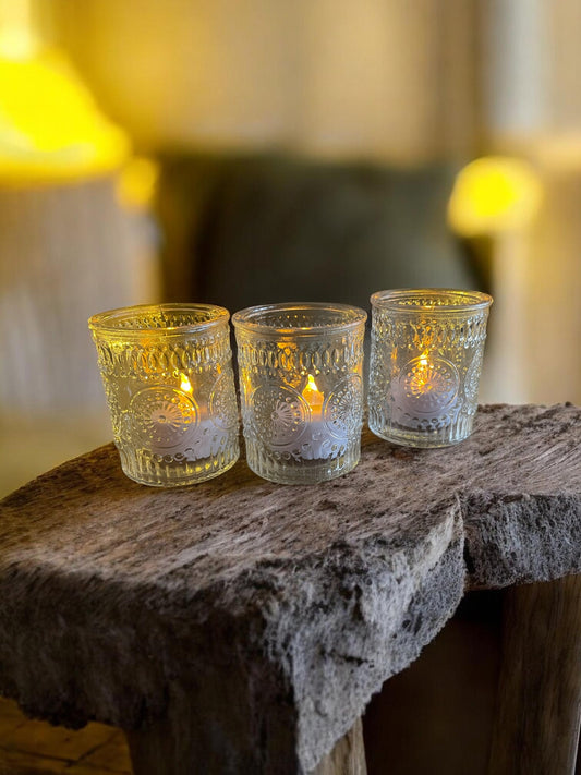 Three lit candles in decorative glass holders on a rustic stone surface with a blurred background.