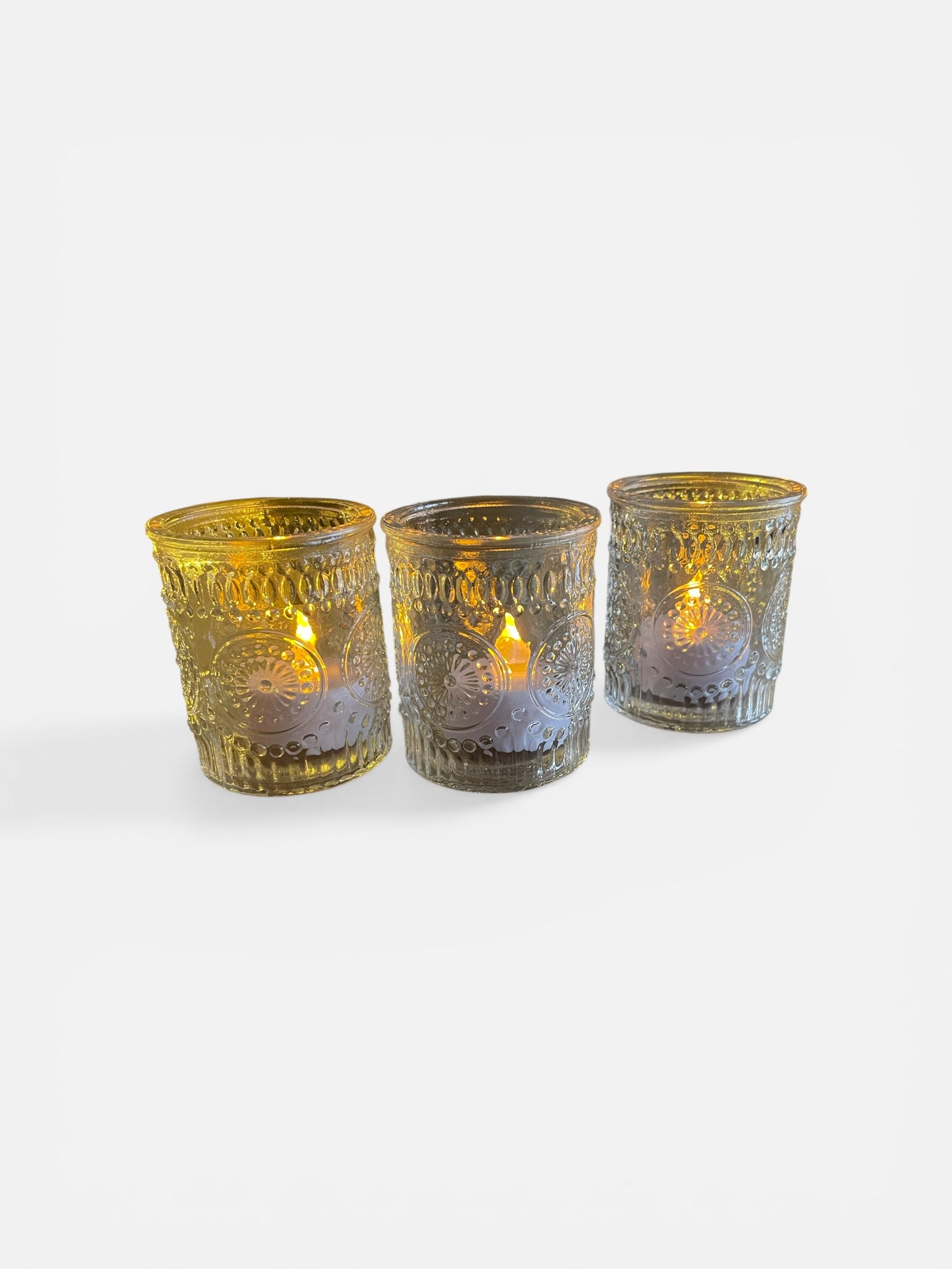 Three decorative glass candle holders with lit candles inside on a white background