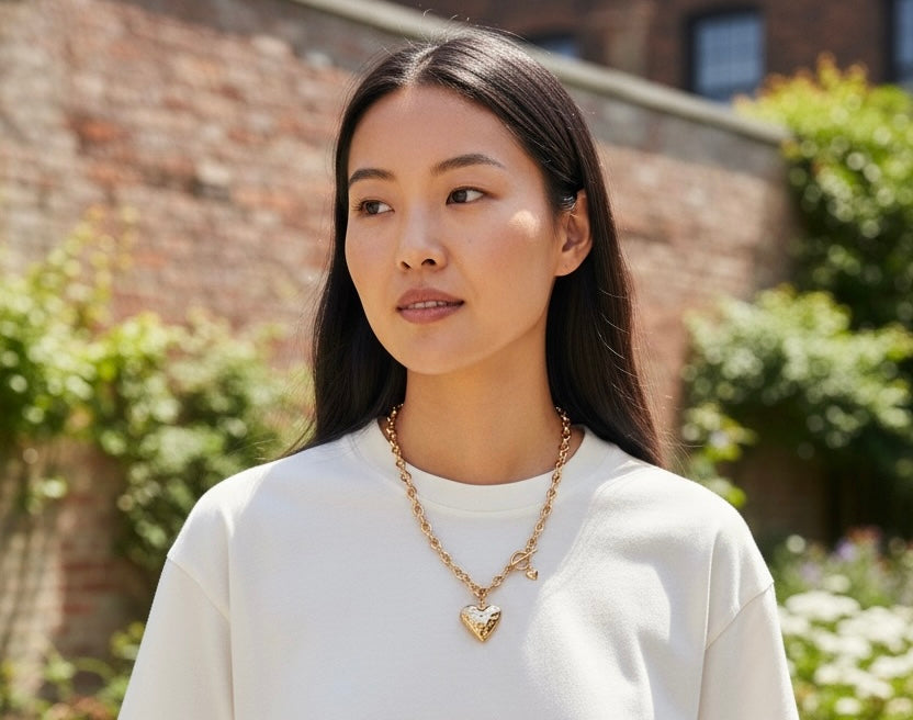 Woman wearing a gold necklace with a heart pendant outdoors.
