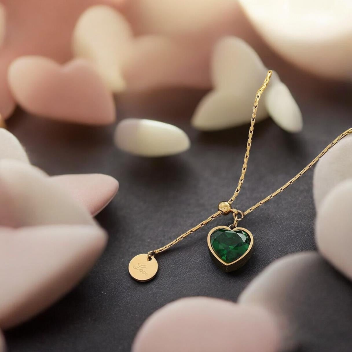 Gold necklace with a heart-shaped emerald pendant on a dark surface.