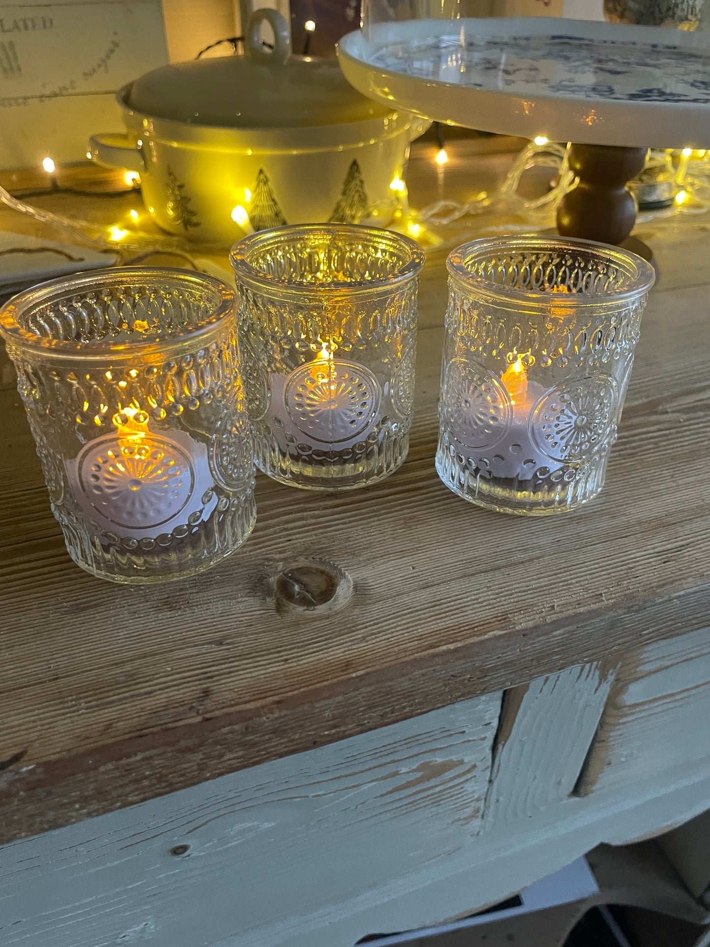 Three glass candle holders with lit candles on a wooden surface.