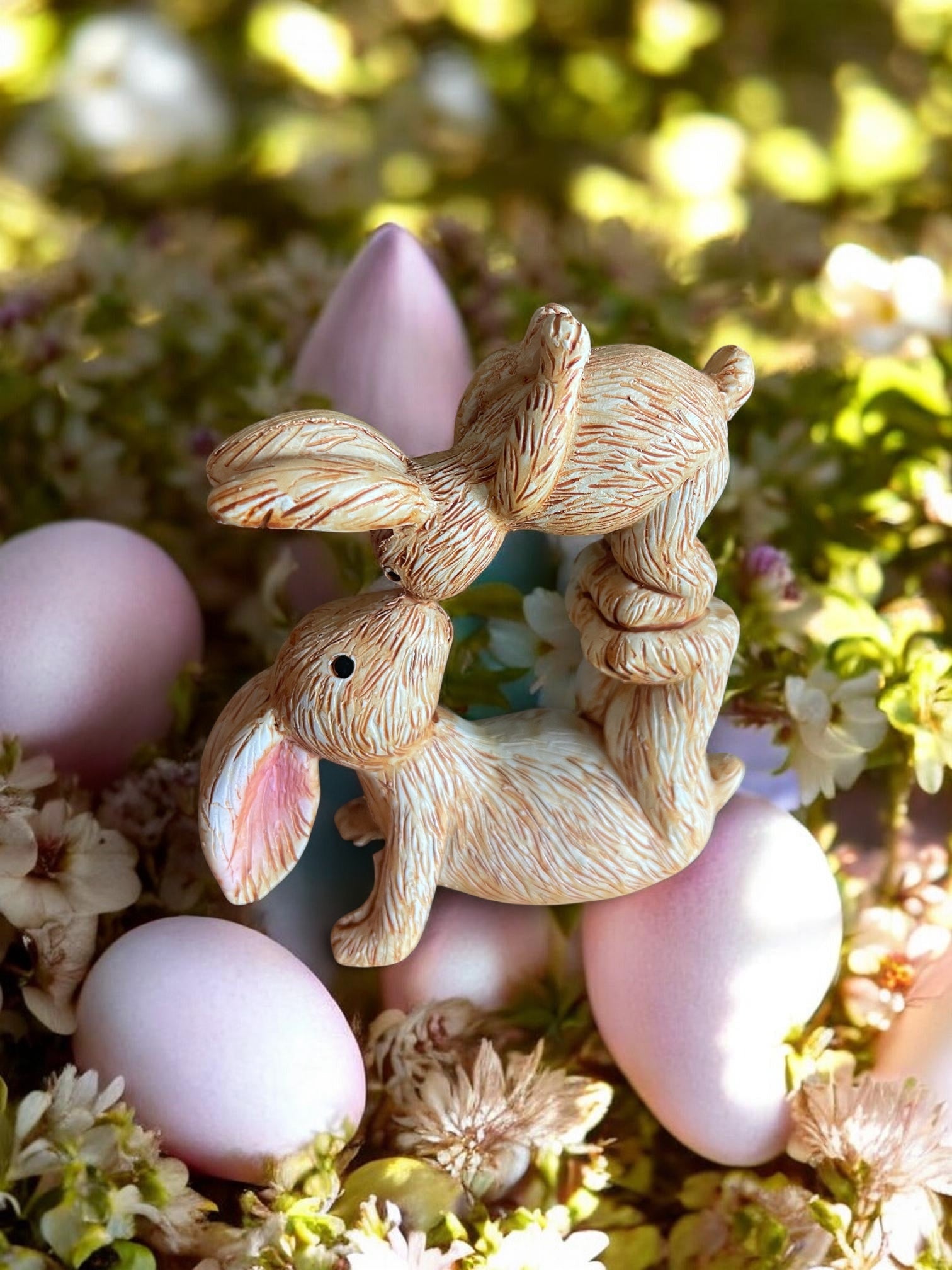 Decorative bunny figurines with Easter eggs and flowers on a blurred natural background