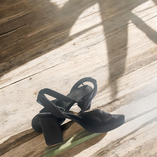 Black sandals on a wooden floor with sunlight casting shadows