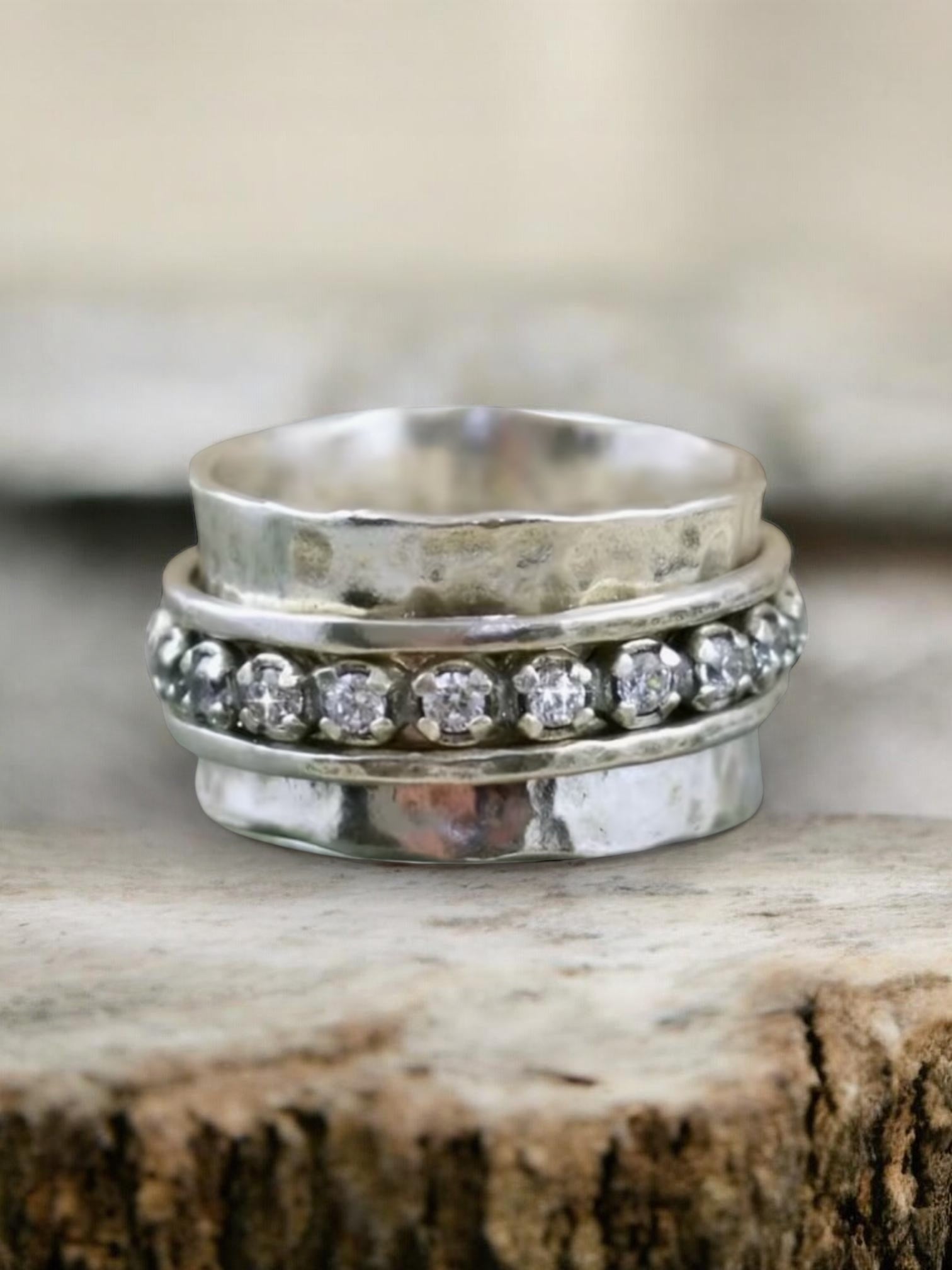 Stack of silver rings with one featuring diamond-like stones on a wooden surface.