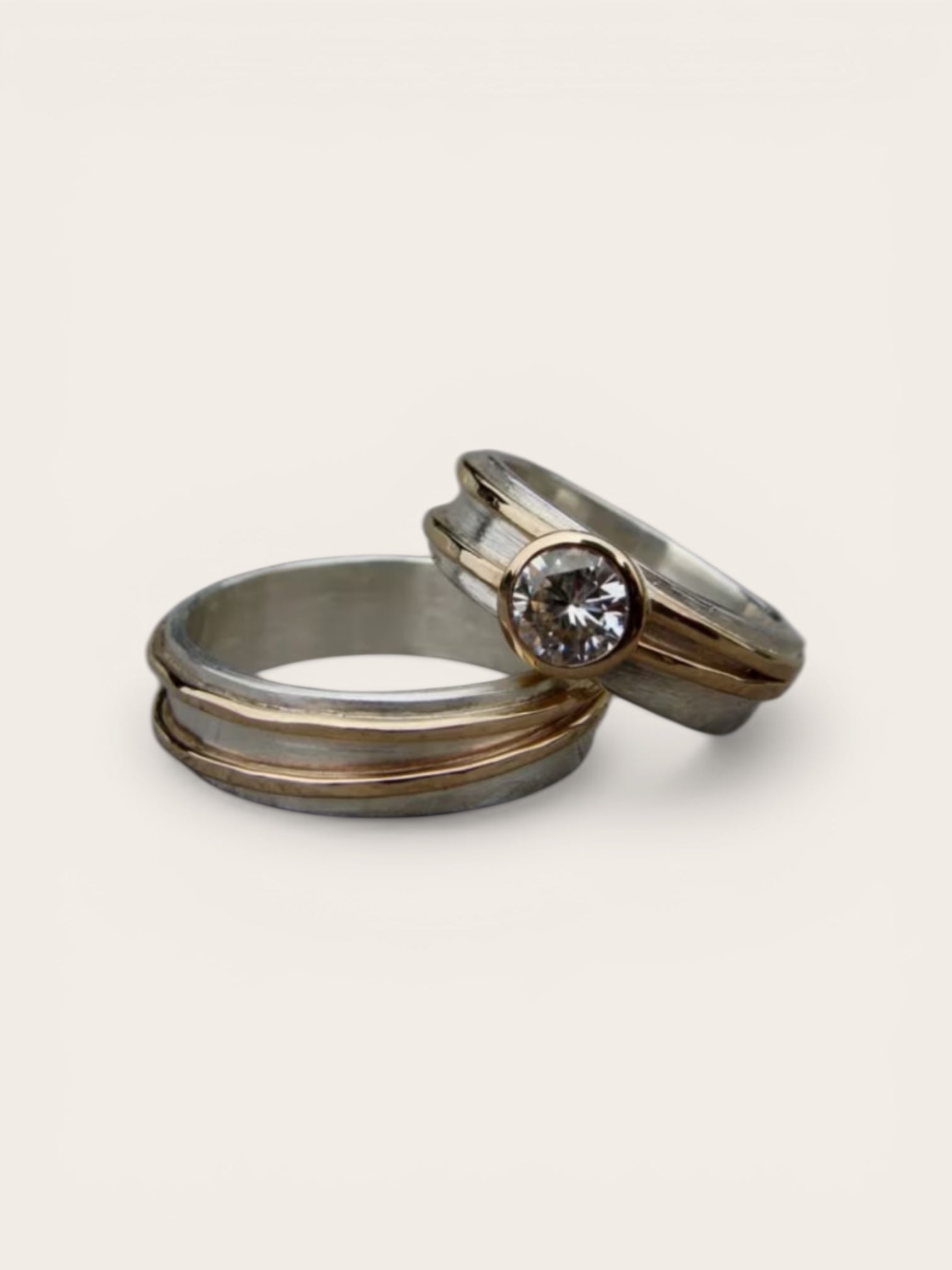 Two metallic rings with one featuring a diamond on a light gray background