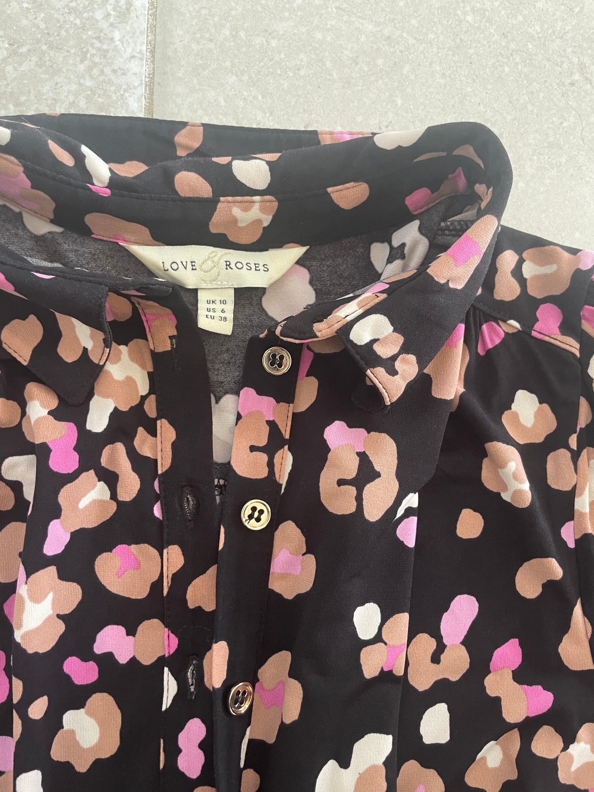 Black shirt with pink and beige abstract pattern on a textured surface