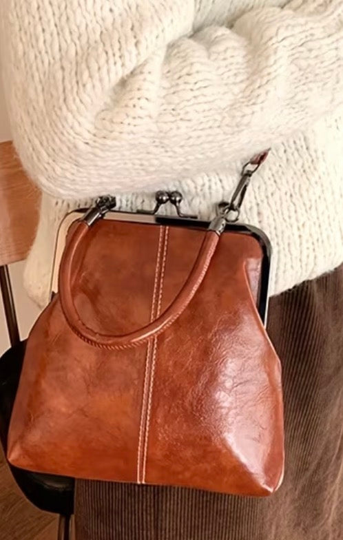 Brown leather handbag held by a person wearing a white sweater.