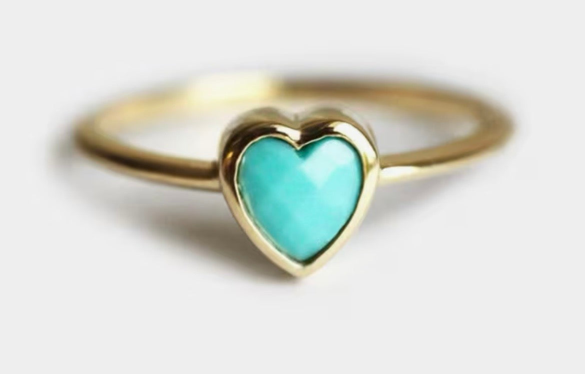 Gold ring with a turquoise heart-shaped stone on a light gray background