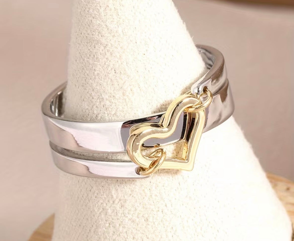 Silver ring with a gold heart-shaped design on a white stand.