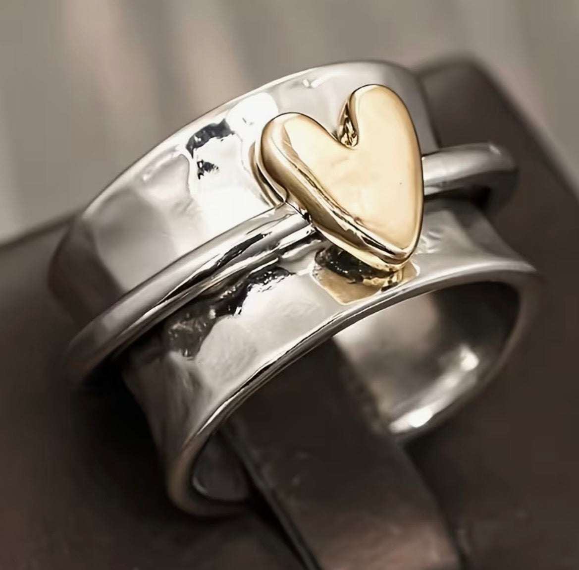 Silver ring with a gold heart-shaped emblem on a dark surface