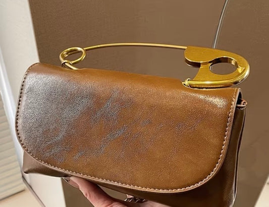 Brown leather handbag with a gold handle held against a neutral background