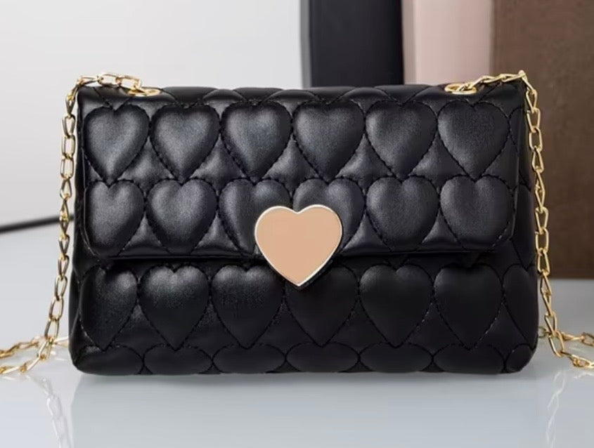 Black quilted handbag with a gold chain and heart-shaped clasp on a white surface.