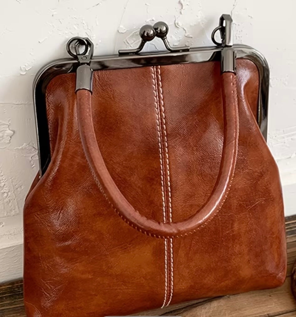 Brown leather handbag with metal clasp on a wooden surface.