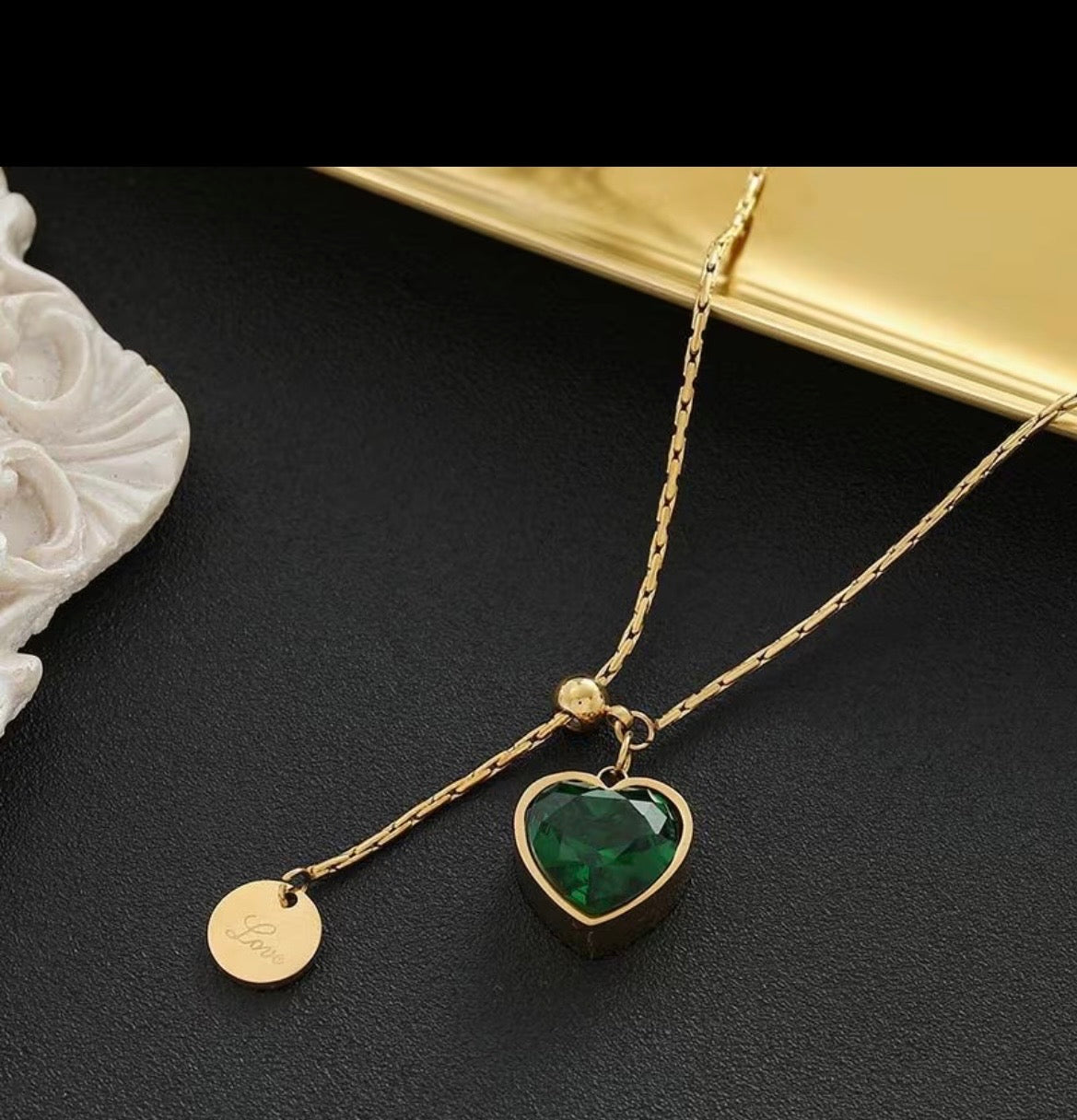 Gold necklace with a green heart pendant on a dark surface