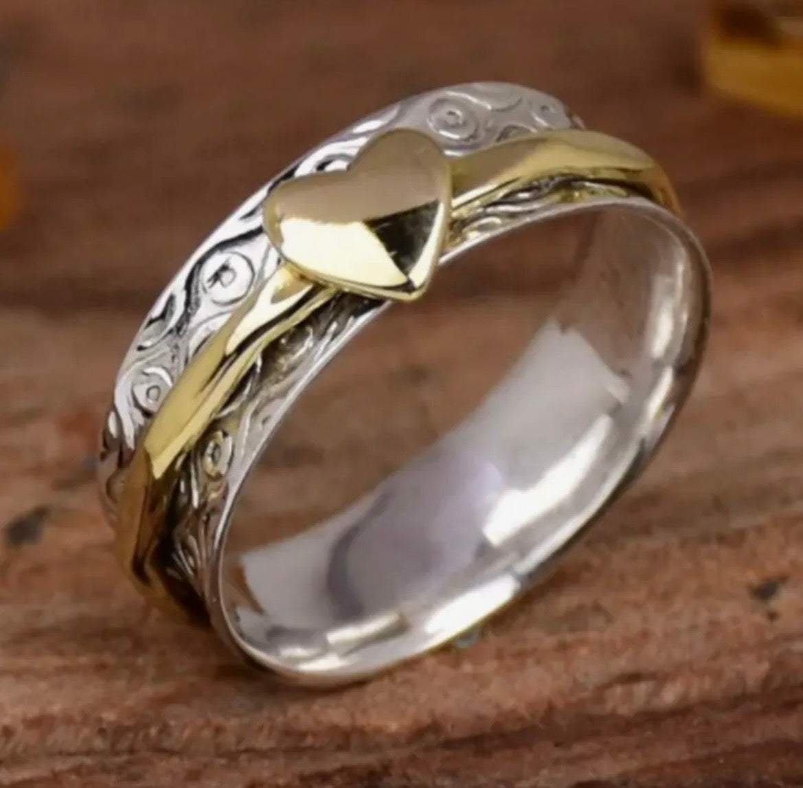 Gold and silver ring with heart design on a wooden surface