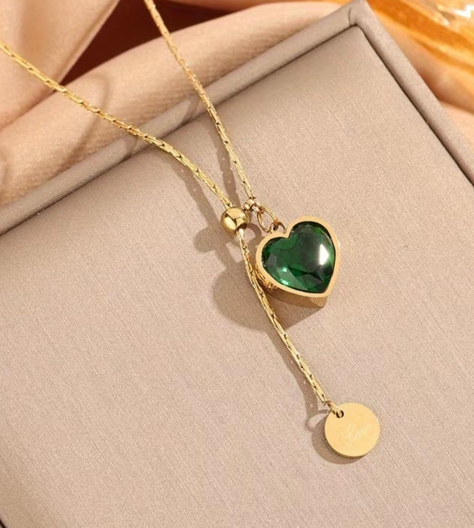 Gold necklace with a green heart pendant on a beige surface