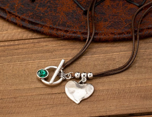 Necklace with heart pendant and green gemstone on a wooden surface