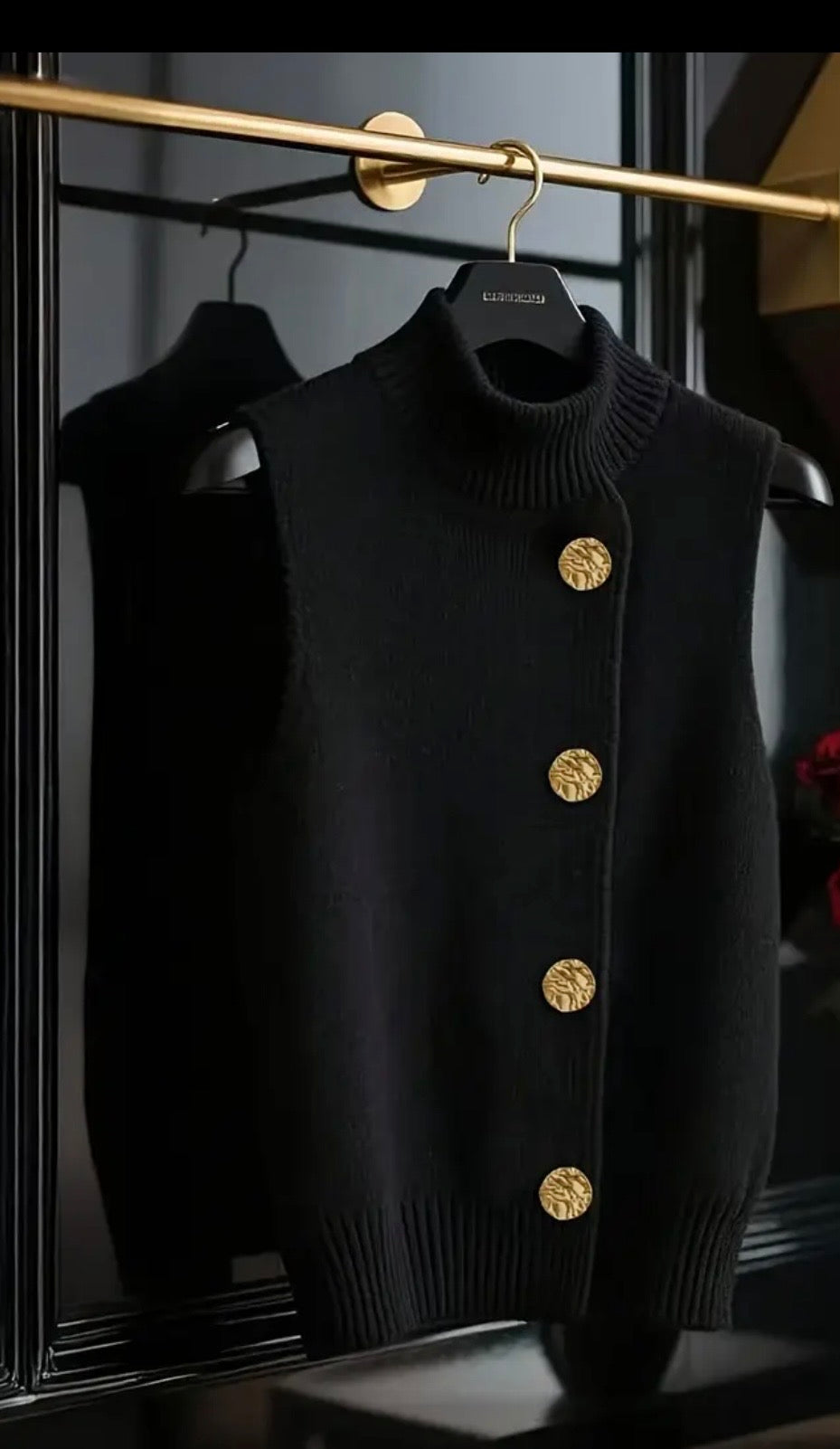 Black sweater vest with gold buttons on a hanger against a dark background
