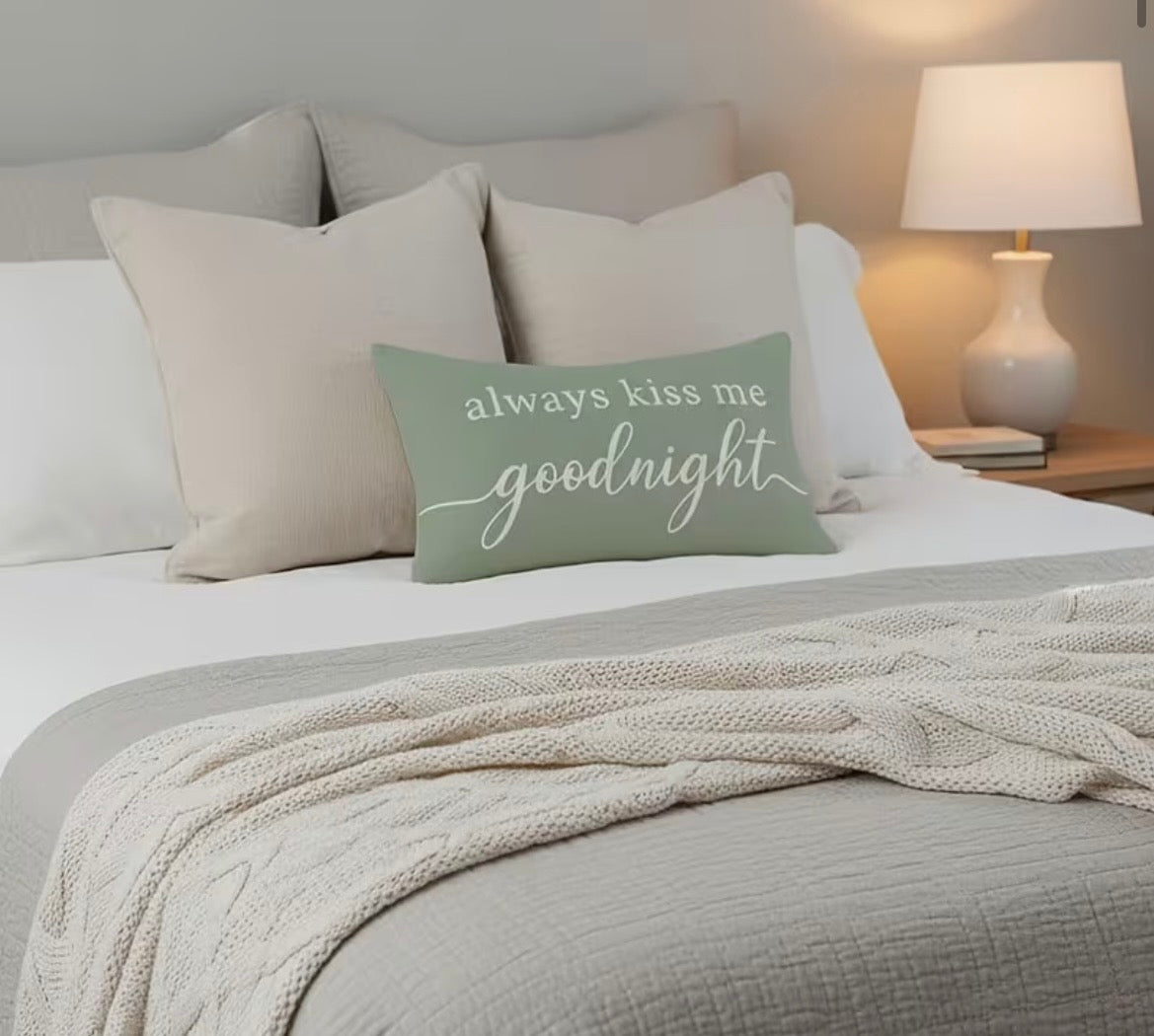 Bedroom with a bed featuring a 'always kiss me goodnight' pillow and a lamp on a nightstand.