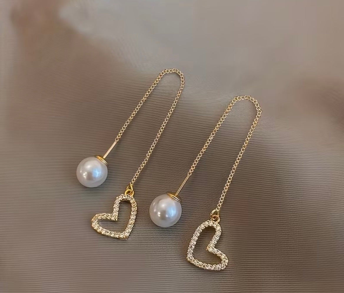 Pair of gold heart-shaped earrings with pearl drops on a beige background