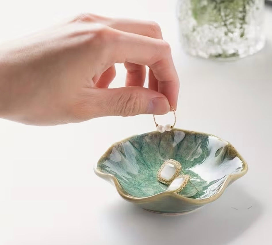 Hand placing a ring into a green ceramic dish on a white surface