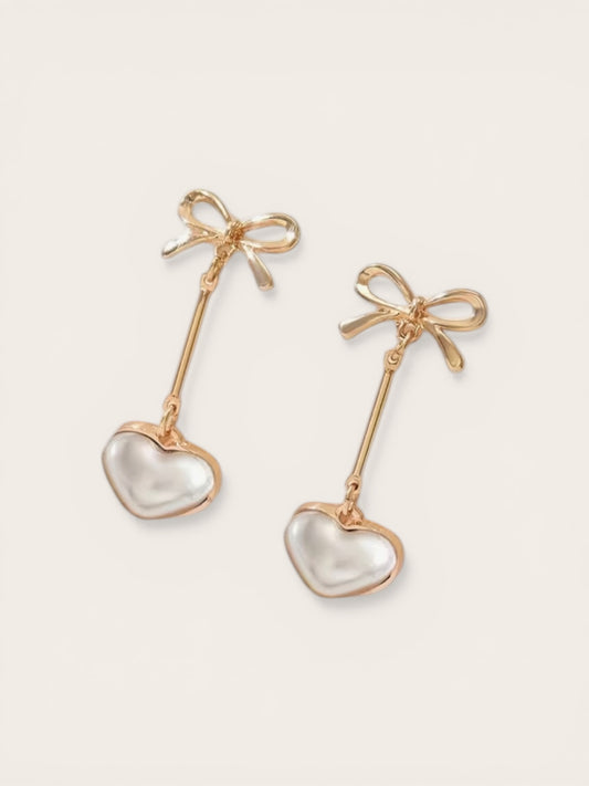 Gold earrings with heart-shaped charms and bow details on a white background
