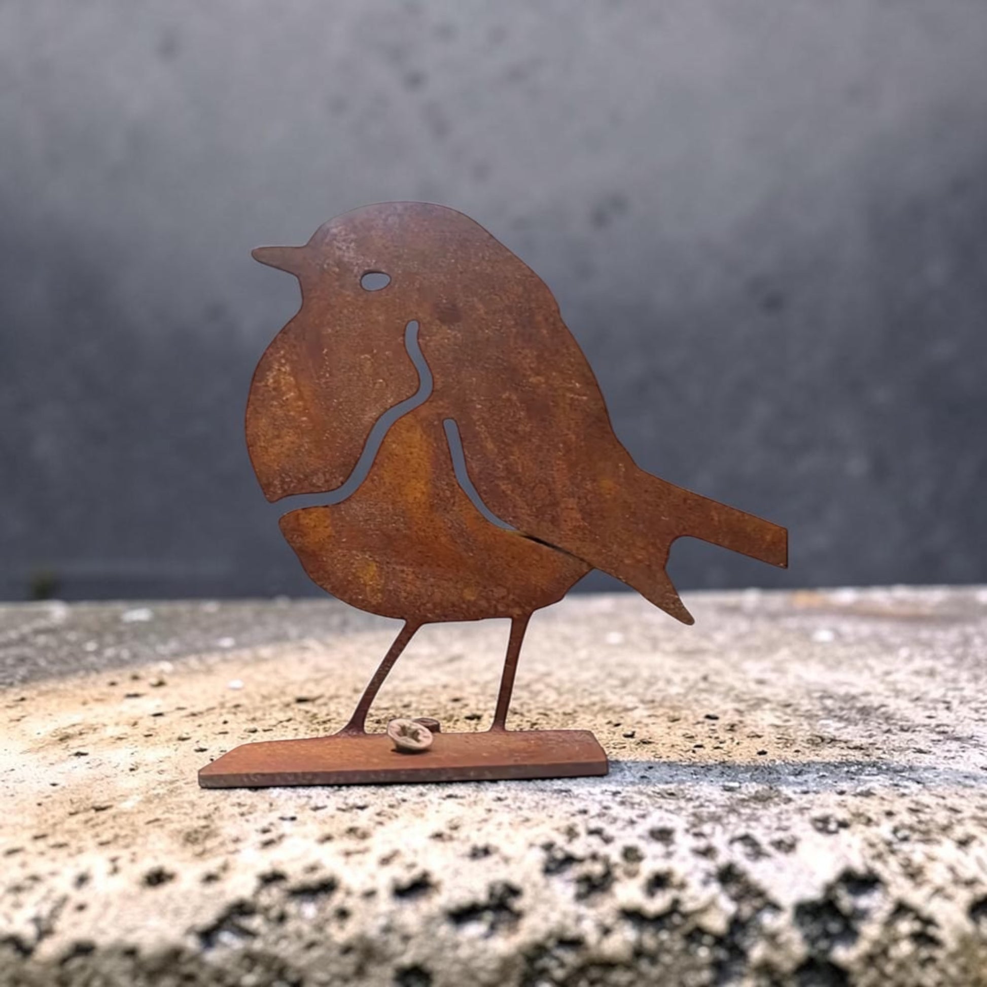 Rust-colored metal bird sculpture on a textured surface with a gray background