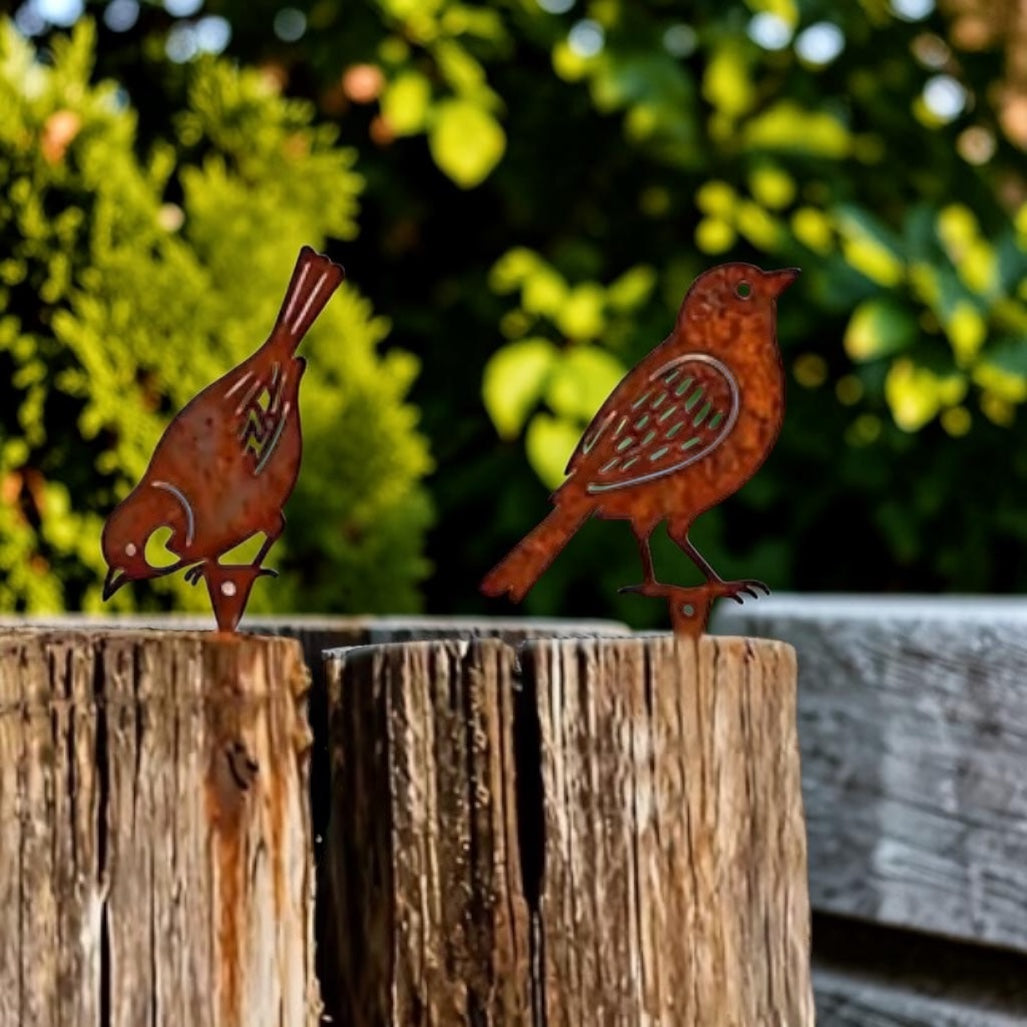 Two rust-colored metal bird sculptures on a wooden post with a blurred green background