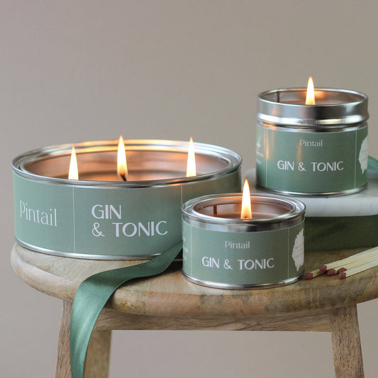 Three 'Gin & Tonic' candles in metal tins on a wooden stand with a plain background.