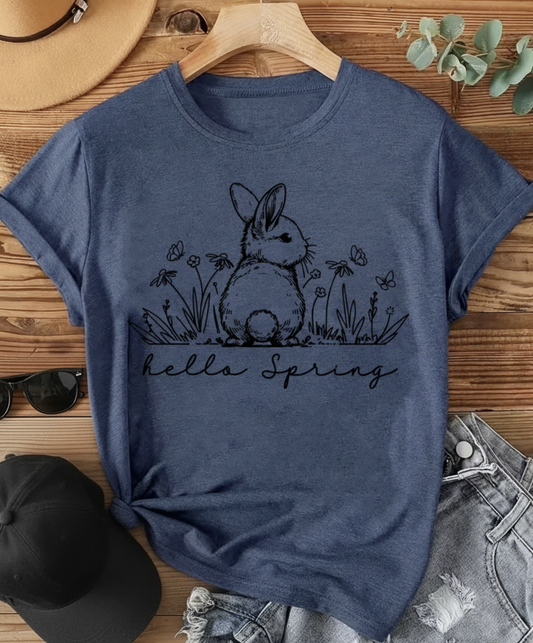 Blue t-shirt with a bunny and 'hello Spring' text on a wooden surface with accessories.